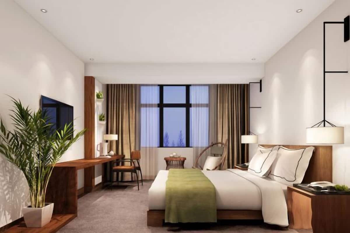 Une chambre d’hôtel moderne équipée d’un lit, de tables de chevet, d’un bureau, d’une chaise, d’une télévision et d’une grande fenêtre avec des rideaux.