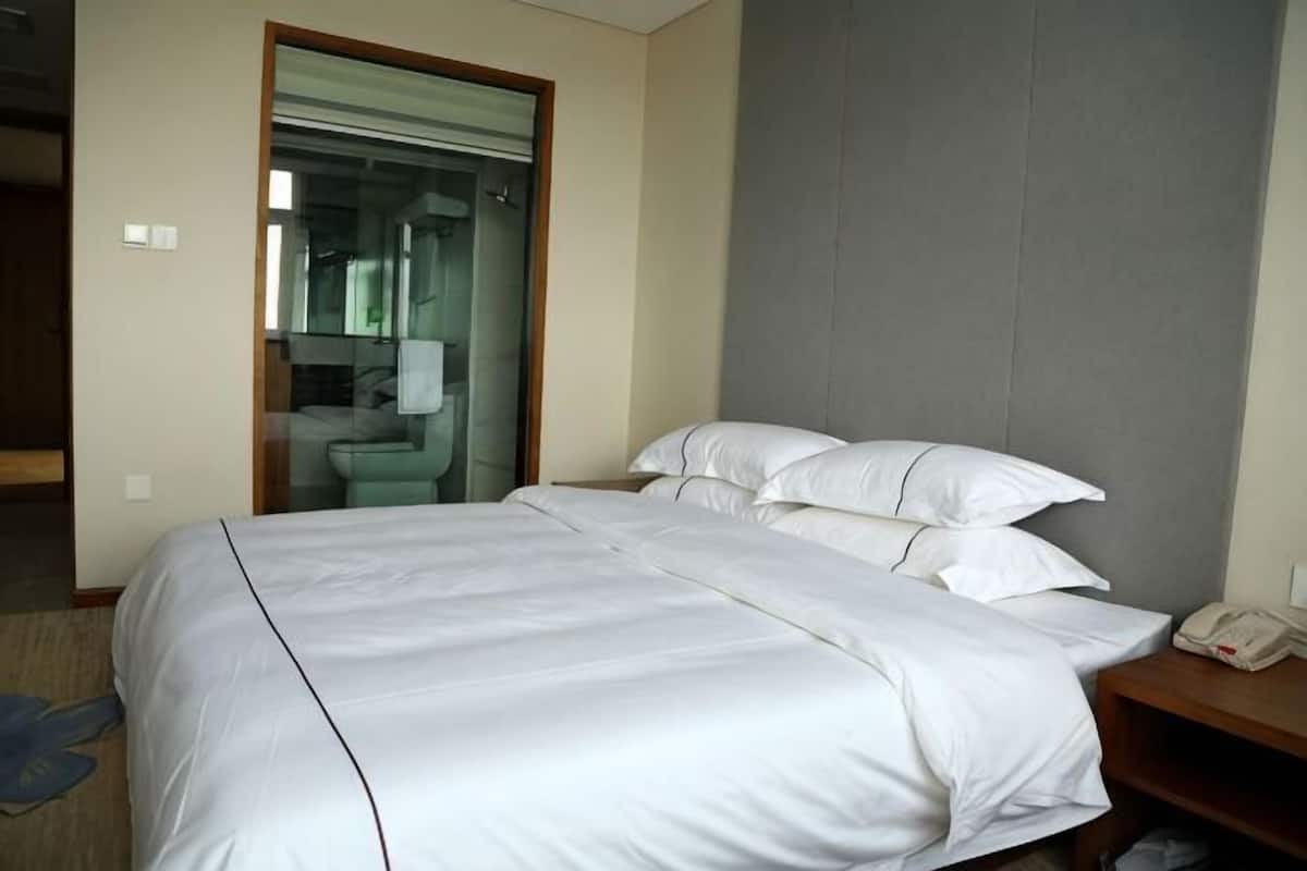 Une chambre d’hôtel avec un grand lit, un téléphone sur la table de chevet et une salle de bain visible à travers une porte ouverte.