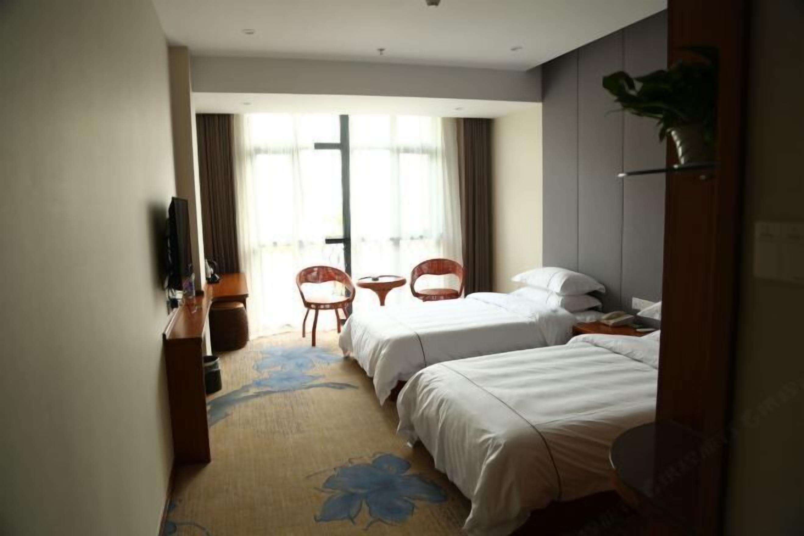 A hotel room with two beds, a TV, a small table, and a chair.