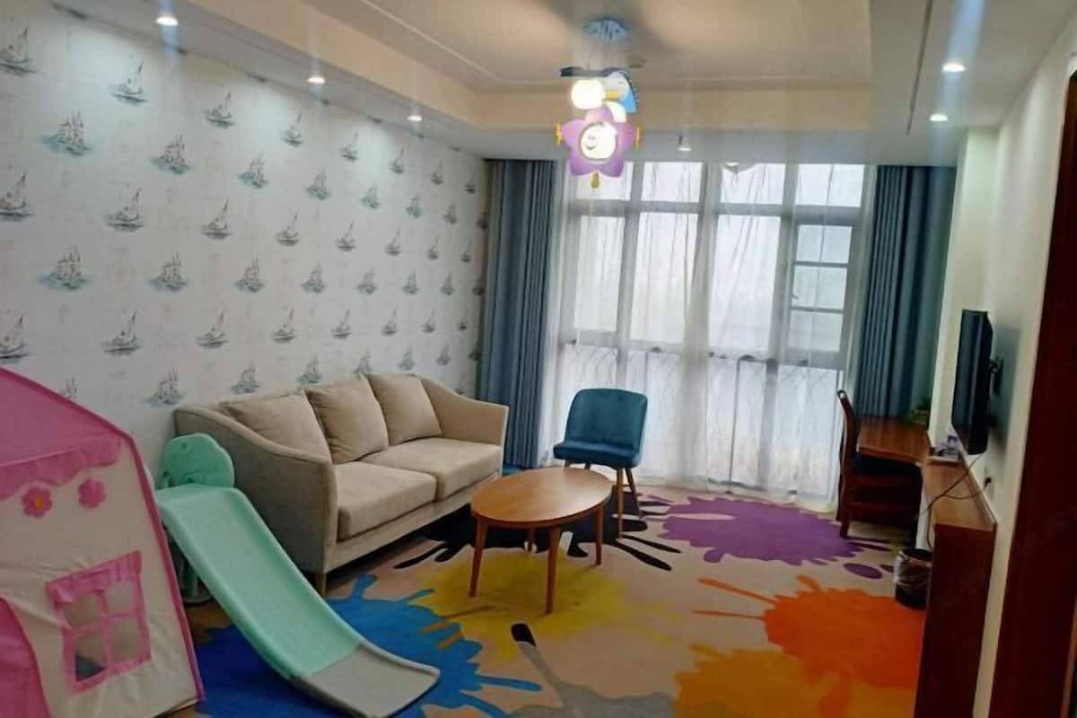 Un salon avec un canapé, une petite table, un fauteuil bleu, un tapis coloré et une tente de jeu.