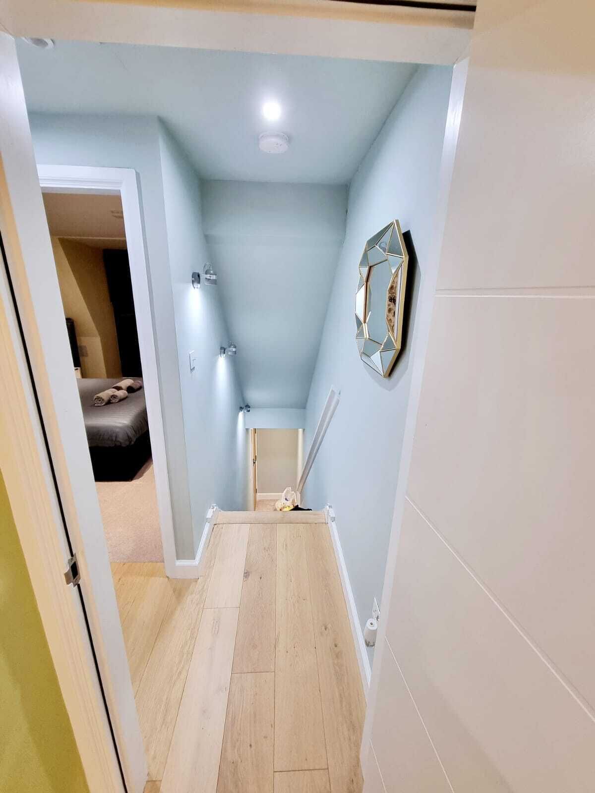 Ein schmaler Flur mit hellblauen Wänden, Holzboden und einem Spiegel an der rechten Wand.