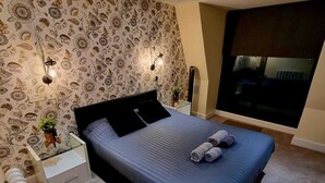 Une chambre à coucher moderne avec un grand lit, un papier peint à motifs, des lampes de chevet et une vue sur la ville la nuit.