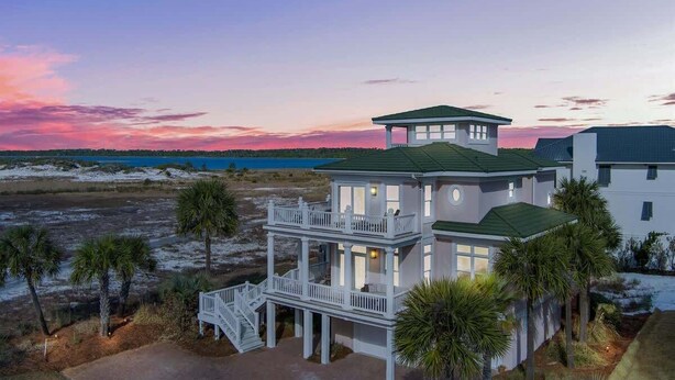 Una casa sulla spiaggia su due piani, con un balcone, un portico coperto e vista sulla spiaggia e sull'oceano.