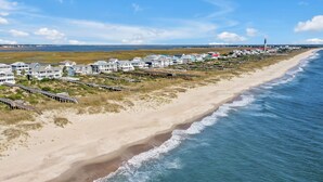 Ett bostadsområde vid kusten med hus som ligger direkt vid stranden, en sandstrand och en brygga.