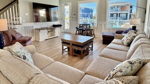 Un salon spacieux avec un plafond en bois, une grande télévision et une vue sur un immeuble par les fenêtres.