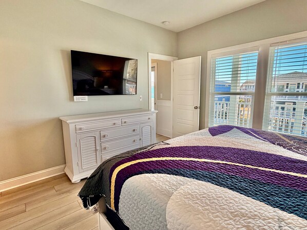 A bedroom with a bed, a dresser, a television, and a door leading to a balcony.
