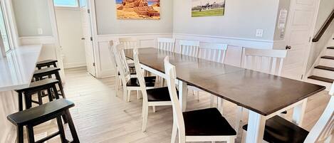 A dining area with a long table, white chairs, and a wooden bench.
