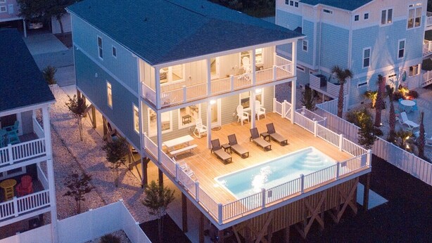 Une maison à deux étages dotée d’une grande terrasse et d’une piscine.