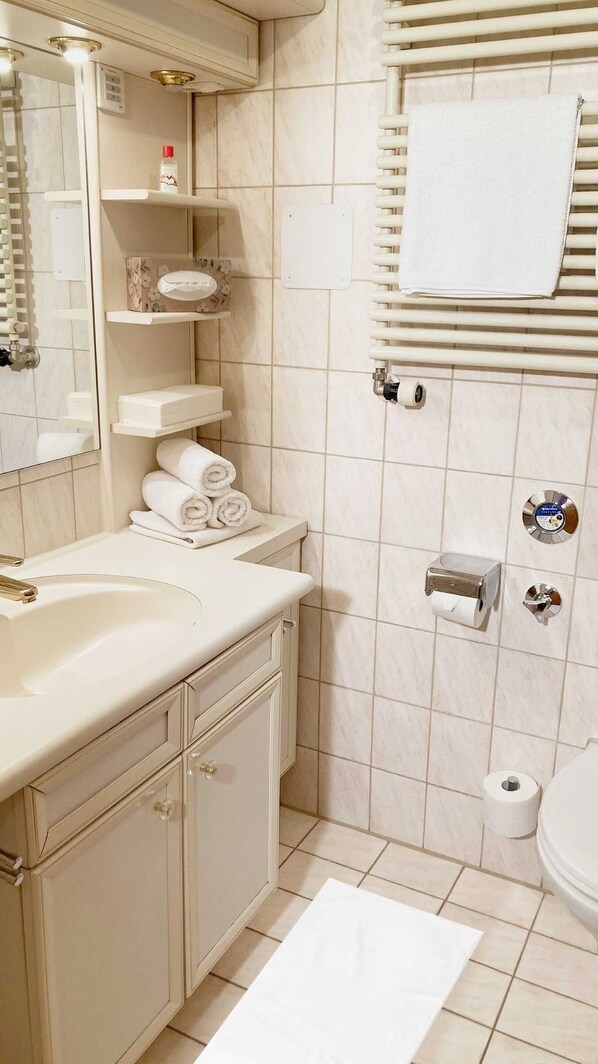A bathroom with a sink, mirror, towel rack, toilet, and a shower area.