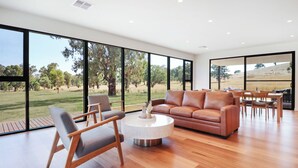 A spacious living room with a large window overlooking a grassy landscape. - Lawson Lodge - Modern home minutes from Lake Eildon (Mansfield)