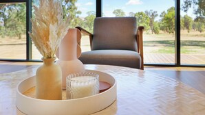 A room with a large window, a chair, a table with a vase and candle, and a view of trees and sky. - Lawson Lodge - Modern home minutes from Lake Eildon (Mansfield)