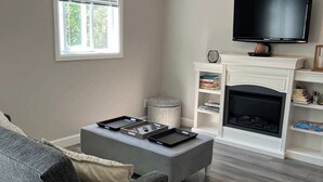 A living room with a grey sofa, a coffee table, a fireplace, a television, and a ceiling fan. - Lake Simcoe Beach Oasis with Backyard and Firepit (Willow Beach)