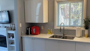 A modern kitchen with white cabinets, a built-in oven, a red coffee maker, and a window with blinds. - Lake Simcoe Beach Oasis with Backyard and Firepit (Willow Beach)