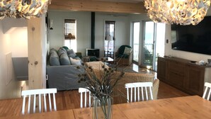 A spacious living room with a large wooden dining table, a sofa, and a television mounted on the wall. - Primehook Beach Bayfront Beauty (Milford)