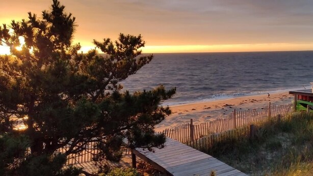 A beach with a wooden walkway leading to a beachside structure with white chairs. - Primehook Beach Bayfront Beauty (Milford)