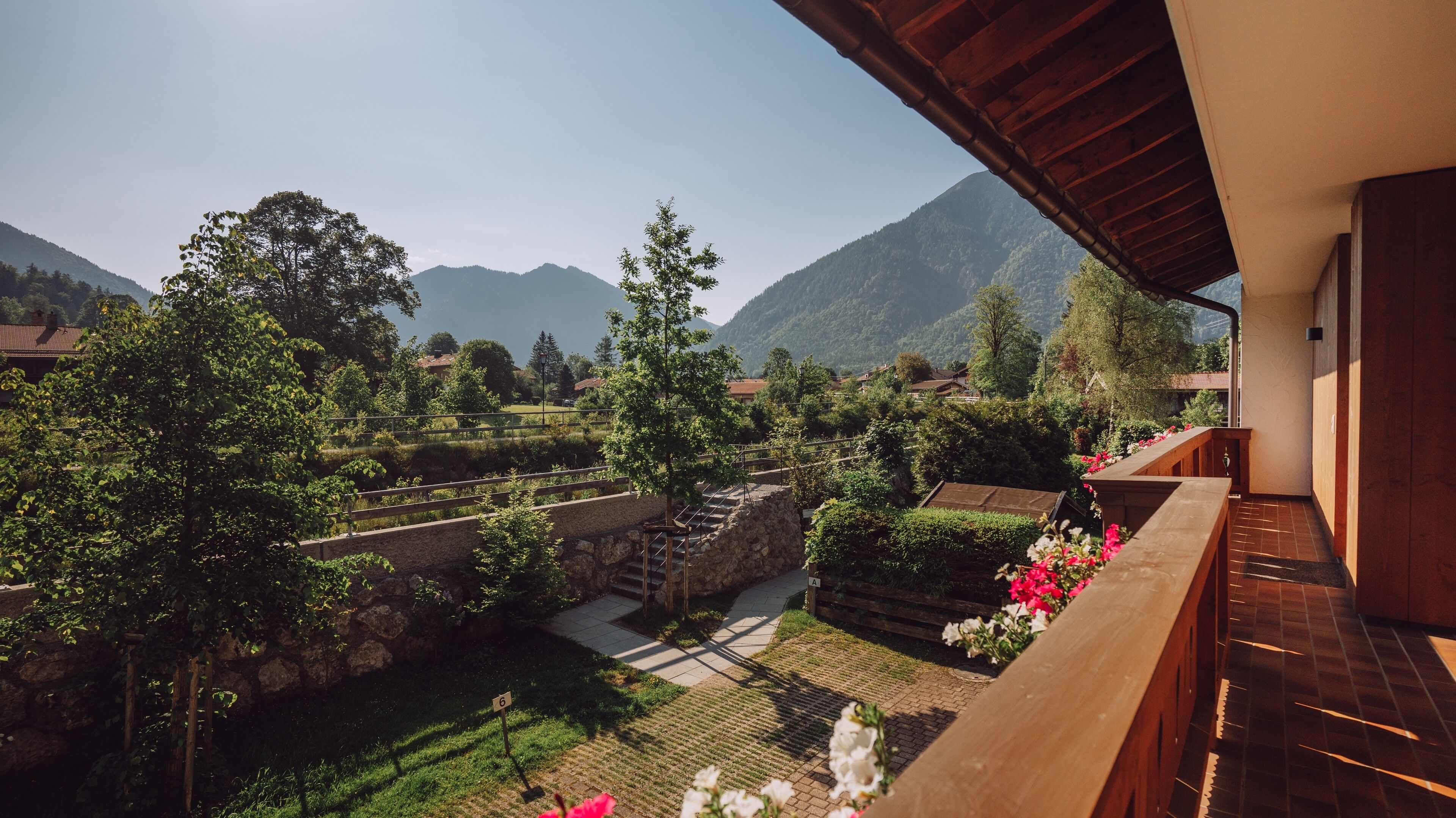 A balcony with a view of a mountainous landscape, a stone staircase, and a garden area with flowers.