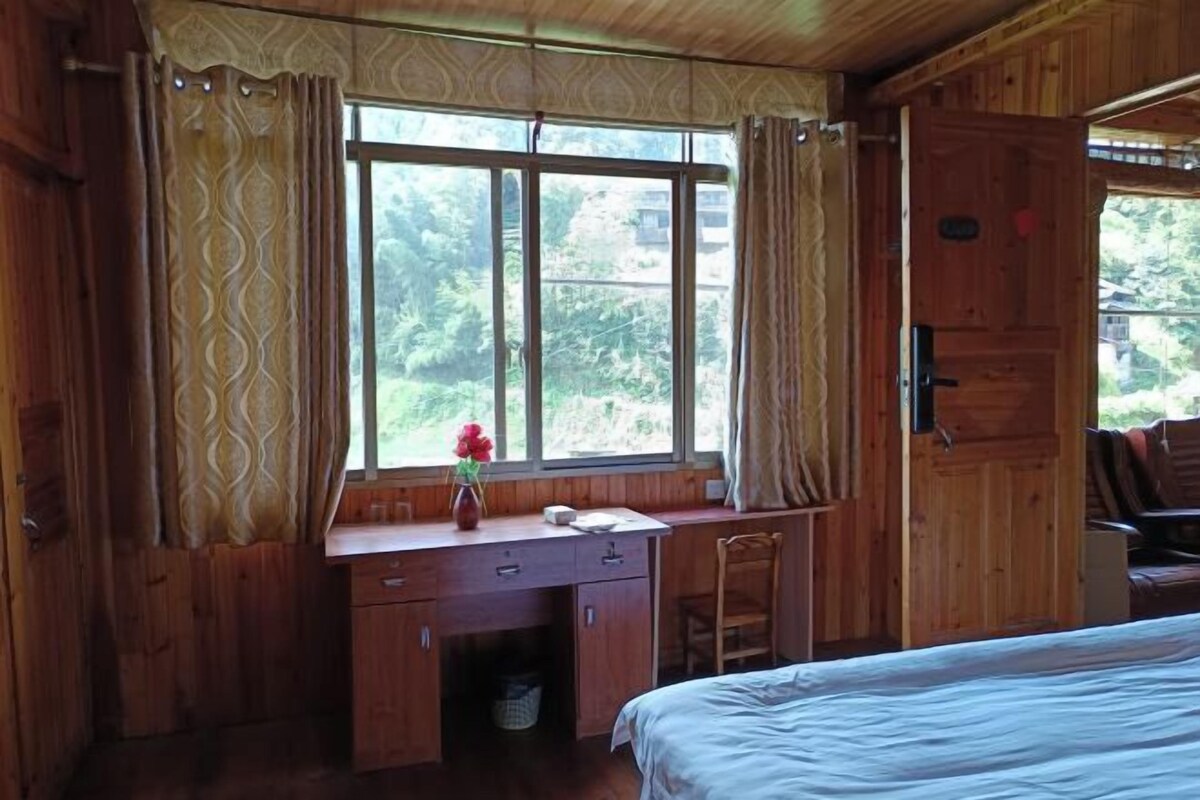 A wooden cabin room with a bed, a desk, and a chair.