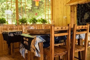 Ein Essbereich aus Holz mit Tischen und Stühlen, Blumentöpfen und einem Fenster mit Blick auf Grünflächen.