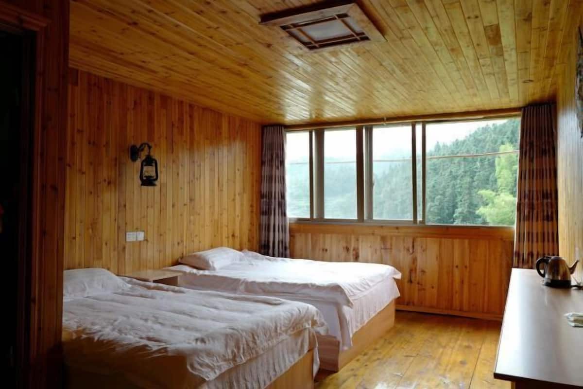 Habitación de cabaña de madera con dos camas, una ventana con vistas al bosque y un hervidor sobre la mesa.