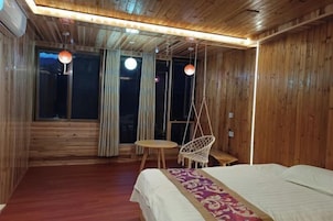 Una habitación de madera con una cama, una silla colgante, una mesita redonda y una ventana con cortinas.