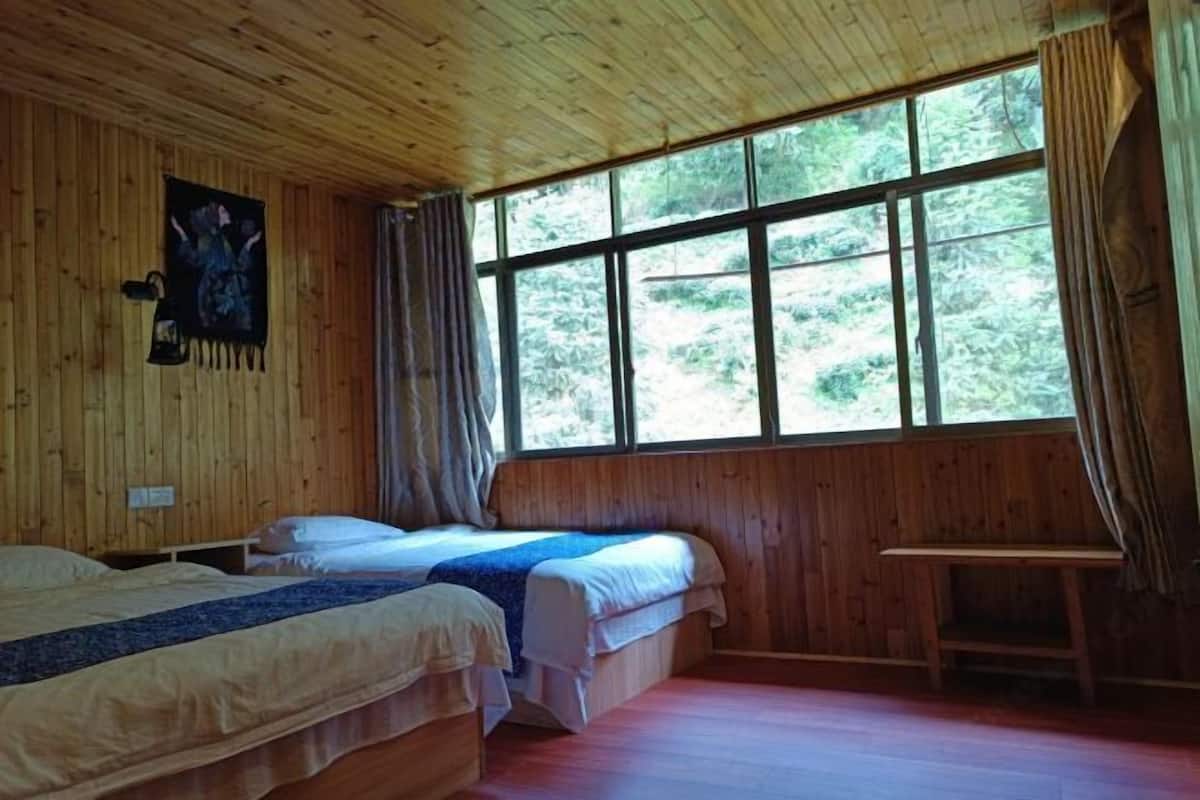 Una habitación de madera con dos camas, una ventana con cortinas y una lámpara fijada a la pared.