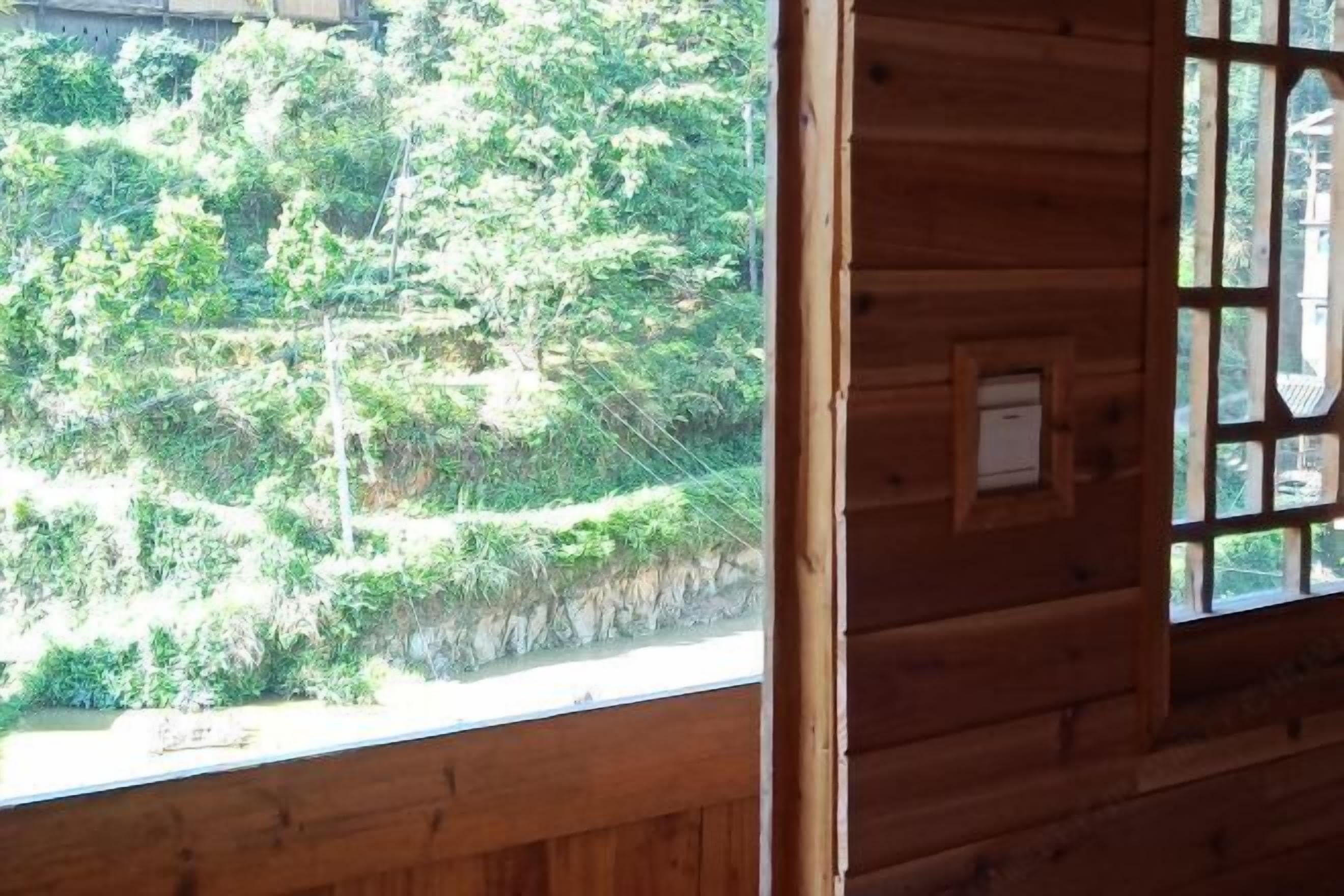 A wooden cabin with a window overlooking a forested hillside.