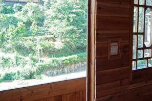 A wooden cabin with a window overlooking a forested hillside. - Tongxiang Country House (Sanjiang)