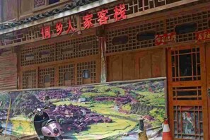 A traditional building with a large mural on the facade, a sign indicating it is a guesthouse, and a scooter parked in front. - Tongxiang Country House (Sanjiang)