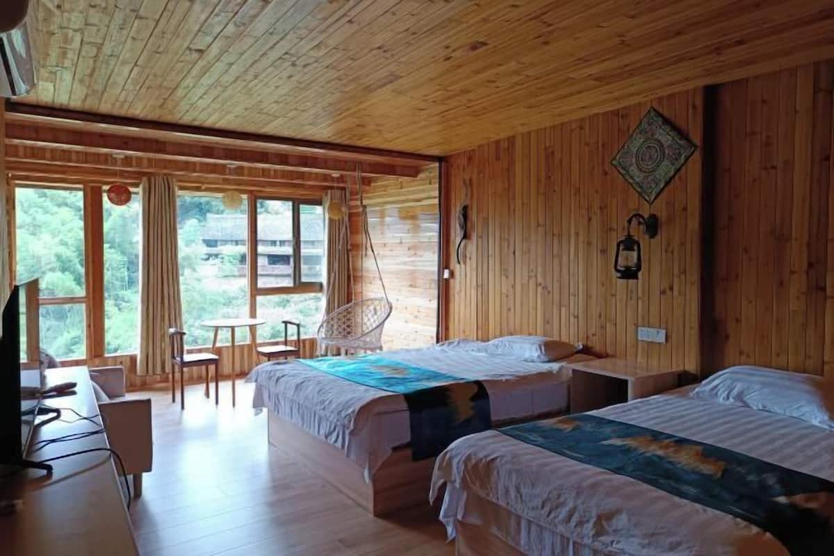 Una cabaña de madera con dos camas, un escritorio, una silla y un ventanal grande.