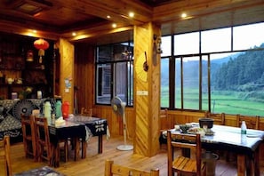 A wooden interior with a dining area, large windows, and a view of a green landscape. - Tongxiang Country House (Sanjiang)