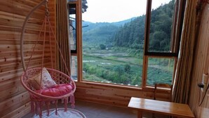 Une pièce en bois avec une grande fenêtre, un fauteuil suspendu avec un coussin et une table en bois.
