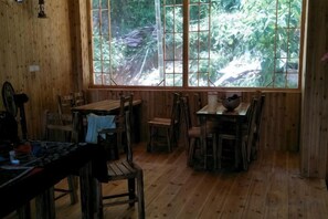 A wooden interior with a large window, multiple tables and chairs, and a rustic ambiance. - Tongxiang Country House (Sanjiang)