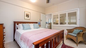 Relax in a serene bedroom with a large bed, wicker chair, and framed picture.