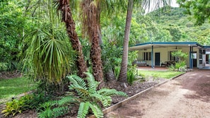 Relax in a serene tropical setting surrounded by lush gardens and a modern, single-story building with a covered porch.