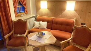 A cozy room with a wooden panel wall, a sofa, two wooden chairs, and a small table with a bowl. - FeWo 16 (Rottach.Apartments) Holiday apartment on Lake Tegernsee (Rottach-Egern)