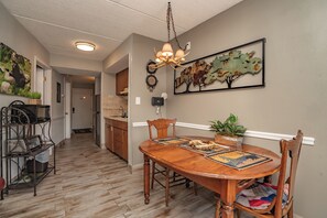 A dining area with a wooden table, chairs, a chandelier, and a wall-mounted decorative piece. - Olde Gatlinburg 109 is a beautiful condo with private balcony located in downtow (Gatlinburg)