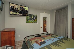 Ein Schlafzimmer mit einem Bett, einem an der Wand befestigten Fernseher, einer Tür und einer kleinen Holzkommode.