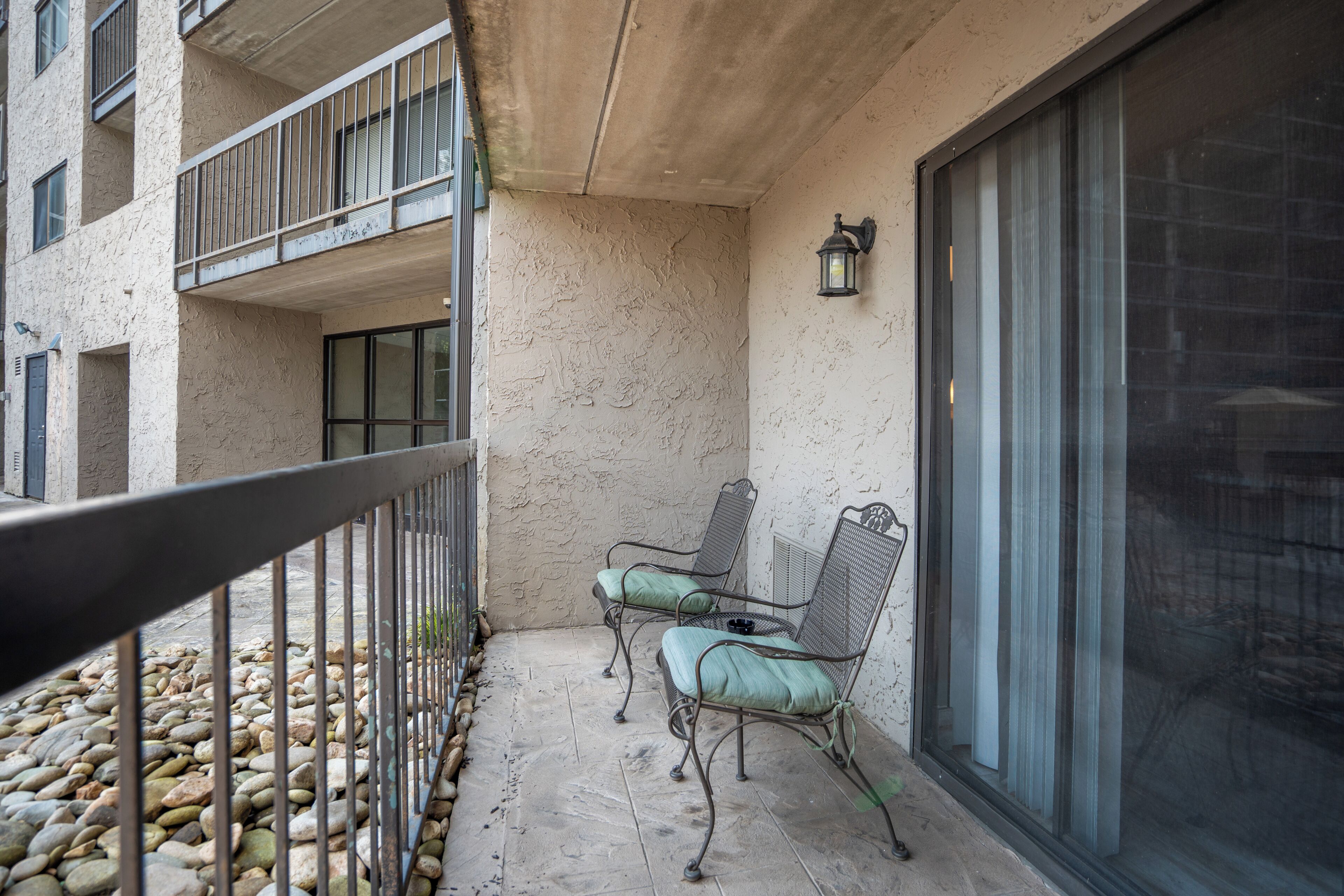 A balcony with a metal railing, two chairs, a small table, and a potted plant.