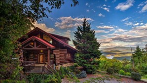 A log cabin with a porch, surrounded by dense greenery and a scenic view of mountains and a lake. - Ahh Time Flies at a mountain cabin with scenic view (Bryson City)