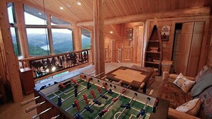 A wooden interior with a foosball table, a sofa, and a view of the outdoors through large windows. - Ahh Time Flies at a mountain cabin with scenic view (Bryson City)