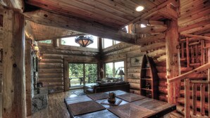 A log cabin interior with a stone fireplace, a dining table with placemats, a sofa, and a staircase. - Ahh Time Flies at a mountain cabin with scenic view (Bryson City)