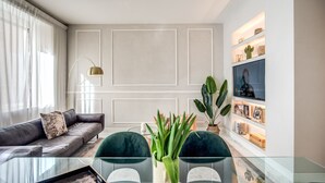 A modern living room with a glass coffee table, dark green chairs, a grey sofa, and a white accent wall with shelves. - Spacious Luxury Family Home - 6 AC / WIFI / Heating / Elevator (Roma)