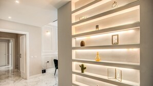 A modern interior with a marble floor, a wall-mounted shelf with various decorative items, and a doorway leading to another room. - Spacious Luxury Family Home - 6 AC / WIFI / Heating / Elevator (Roma)