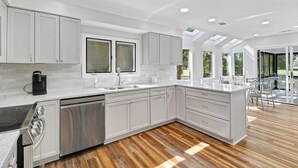 Una cocina moderna con armarios blancos, un lavavajillas de acero inoxidable y una cafetera negra.