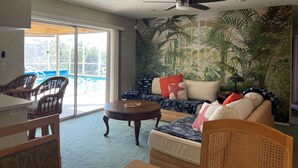 A living room with a ceiling fan, a sofa with patterned cushions, a dining table with chairs, and a view of a pool through large glass doors. - Magical Family Oasis - Diamond Sunsets in Vacation Land -Sleeps10 -Pet Friendly  (Punta Gorda)