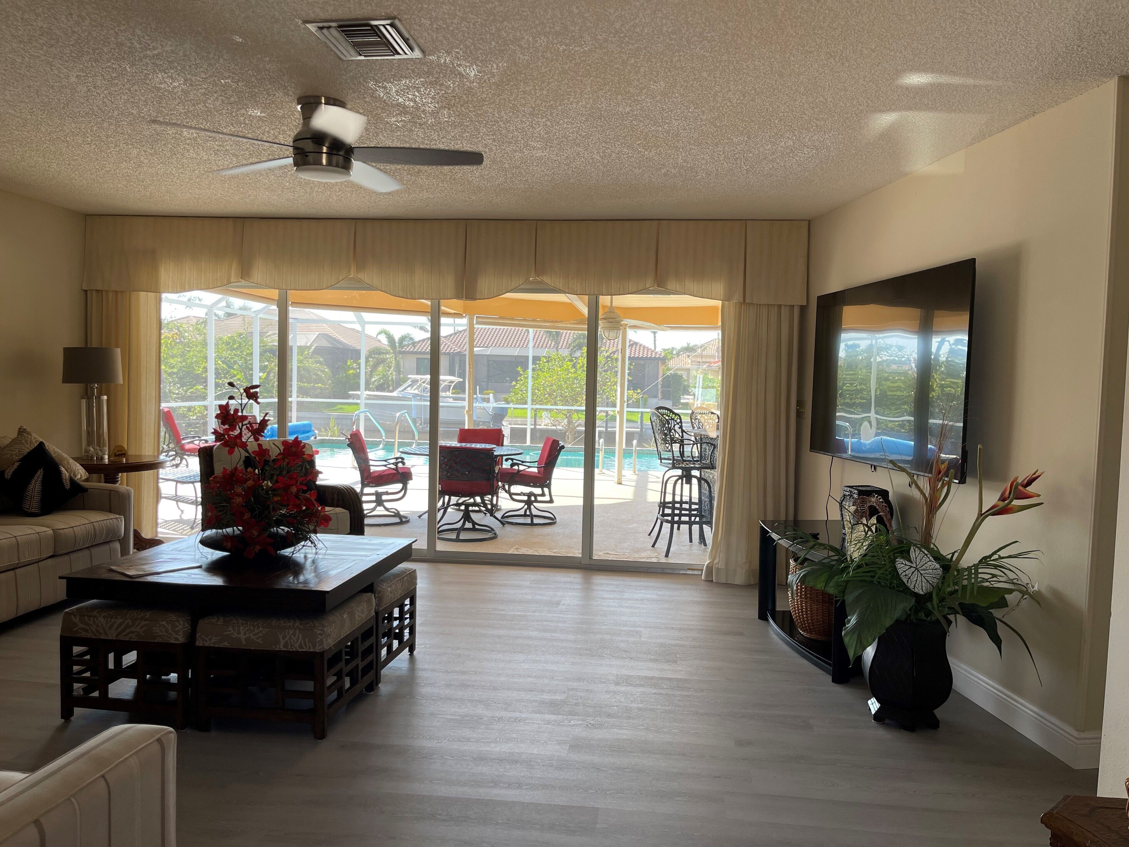 Un vaste salon doté d’un ventilateur de plafond, d’un grand téléviseur et offrant une vue sur une piscine grâce à de grandes portes-fenêtres coulissantes.