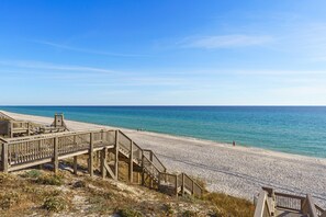 Une plage avec une promenade en bois menant à la rive, un ciel bleu clair et une mer calme.