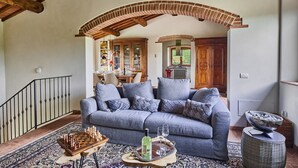 Ein gemütliches Wohnzimmer mit einem grauen Sofa, einem Schachbrett und einer Ablage mit Gläsern und einer Flasche.