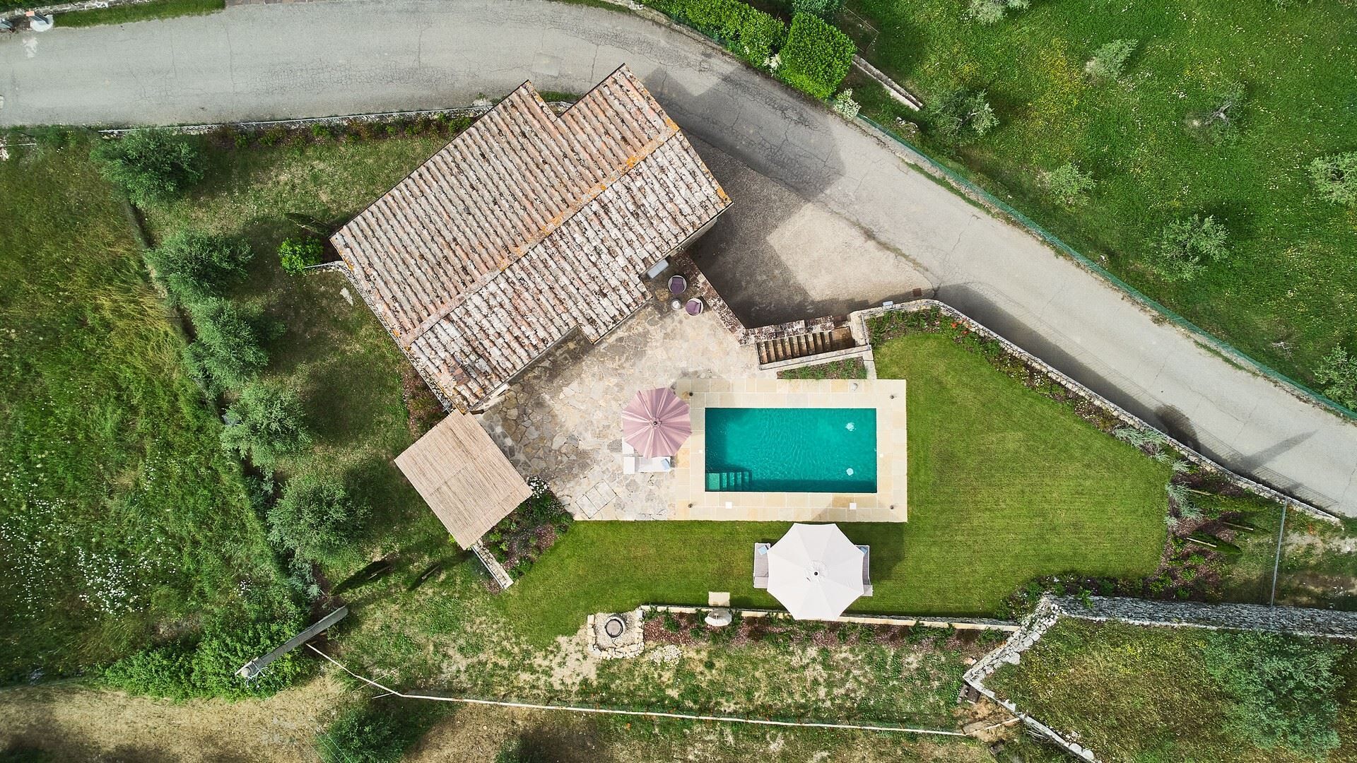 An aerial view of a property with a swimming pool, a patio area, and a fenced garden.