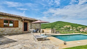 Ein Steinhaus mit Pool, Sitzgelegenheiten im Freien und Blick auf ein Hügeldorf.